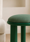 Compact Juntowd upholstered stool used as a bespoke vanity seat or dressing room accent in a luxury bedroom.